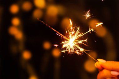 Yeni yılınız kutlu olsun. Işıklı yılbaşı ağacının arka planında bir kadın elinde maytap yanıyor.