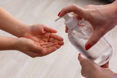 Küçük kıza alkol spreyi sıkan bir kadın. Anne ve kızı el dezenfektanı kullanıyor. Ellerindeki koruma mikropları Covid-19 salgını. Coronavirus, kirlilik koruma konsepti. Evde kal..