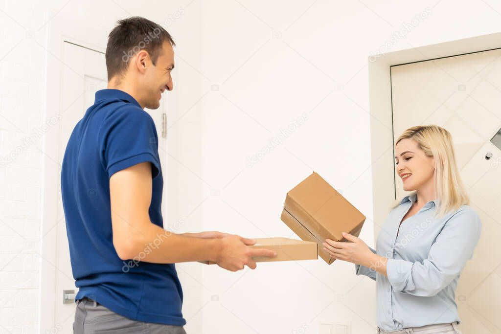 woman receiving boxes from postman at the door in home delivery concept. Woman received the parcel from the postman at home. Postman giving cardboard box to young woman.