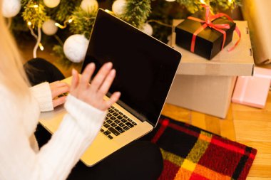 Yılbaşı ağacının arka planında dizüstü bilgisayarı olan kadın internetten mutlu Noeller diliyor.
