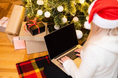 Kanepede oturan güzel sarışın bir kadının fotoğrafı. Yılbaşı hediyesi olarak bilgisayar kullanıyor..