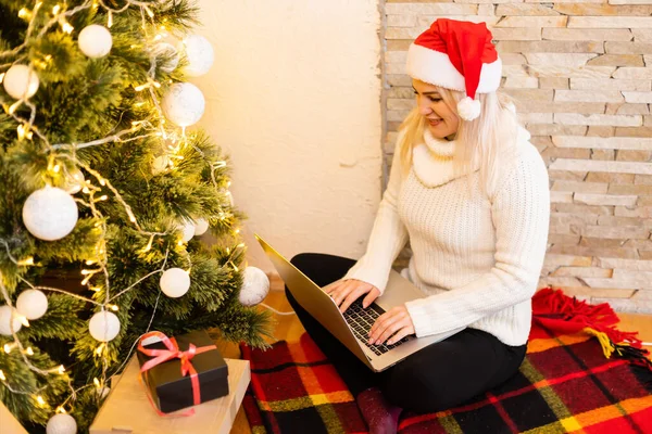 크리스마스 트리를 배경으로 랩탑을 가지고 여성이 온라인으로 크리스마스 축하를 받는다 — 스톡 사진
