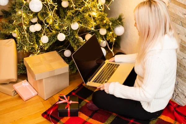 아름다운 금발의 여성이 크리스마스 선물을 노트북을 사용하며 소파에 — 스톡 사진