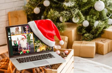 Bilgisayar rahat odasında, kırmızı şapkalı ve Noel Baba ekranda Mutlu Noeller ve mutlu yıllar diliyor.