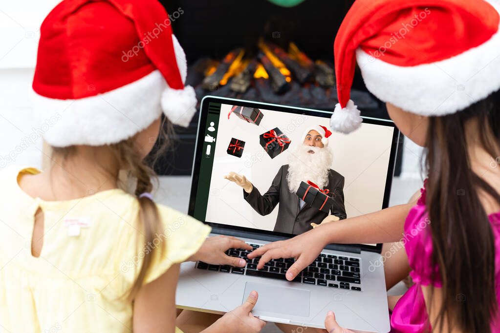A group of children watching a video chat with Santa using a laptop in a decorated room during Christmas. girls 8-9 years talking with Santa Claus have a computer camera in a home.