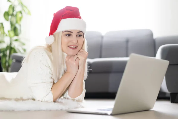 赤いサンタクロースの帽子をかぶっている若い笑顔の女性クリスマスの日に家族や友人とのソーシャルネットワーク上でビデオ通話を行う — ストック写真