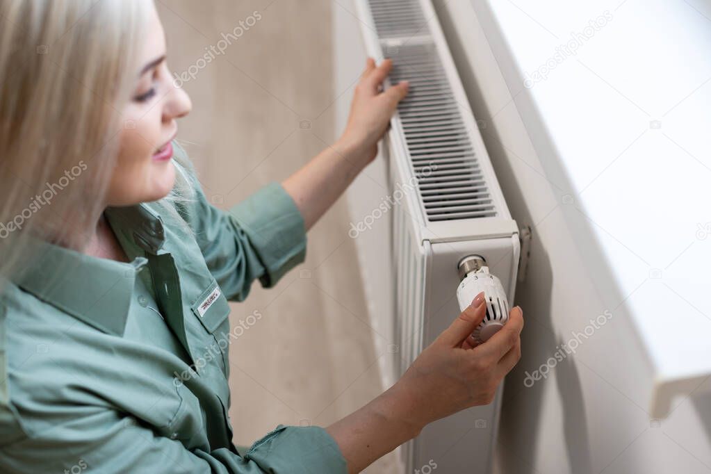 Young and beautiful blond woman touching the radiator. Heating season concept.