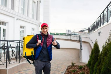 Dışarıdaki yiyecek teslimatı için sarı termo çantalı neşeli bir teslimatçının portresi.