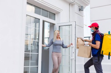 Termal sırt çantalı kurye genç bir iş kadınına taze yemek getiriyor. Restoran yemeği teslimatı konsepti