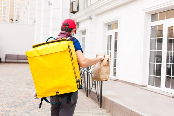 Delivery Man standing with yellow thermo backpack for food delivery near the entrance home with empty space to copy paste