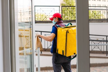 Evin girişinde termo çantalı genç bir kurye. Yemek dağıtım servisi.