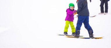 Eğitmenler kar yamacındaki bir çocuğa snowboard yapmayı öğretiyor.