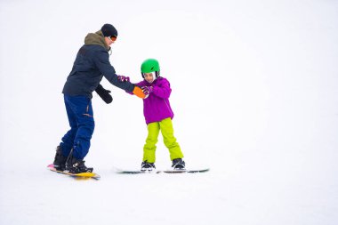 Eğitmenler kar yamacındaki bir çocuğa snowboard yapmayı öğretiyor.