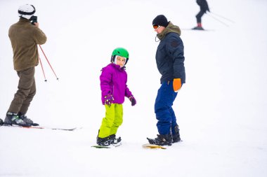 Eğitmenler kar yamacındaki bir çocuğa snowboard yapmayı öğretiyor.