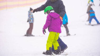 Eğitmenler kar yamacındaki bir çocuğa snowboard yapmayı öğretiyor.