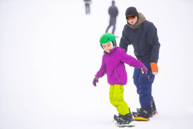 Eğitmenler kar yamacındaki bir çocuğa snowboard yapmayı öğretiyor.