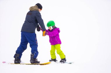 Eğitmenler kar yamacındaki bir çocuğa snowboard yapmayı öğretiyor.