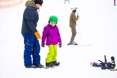 Eğitmenler kar yamacındaki bir çocuğa snowboard yapmayı öğretiyor.