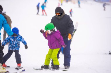 Eğitmenler kar yamacındaki bir çocuğa snowboard yapmayı öğretiyor.