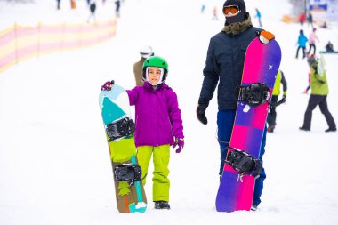 Eğitmenler kar yamacındaki bir çocuğa snowboard yapmayı öğretiyor.