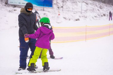 Eğitmenler kar yamacındaki bir çocuğa snowboard yapmayı öğretiyor.