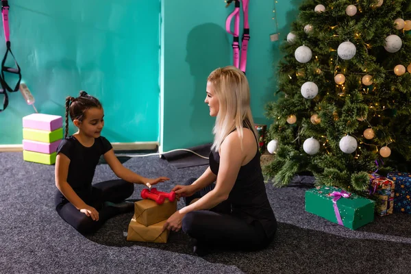 sports mother and daughter unpack fitness gifts near the christmas tree