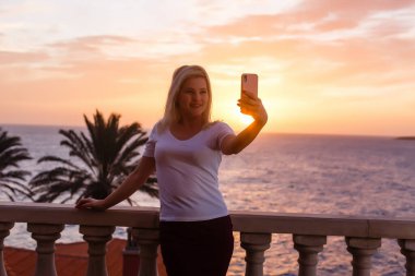 Balkondan gün batımına hayran bir kadın.