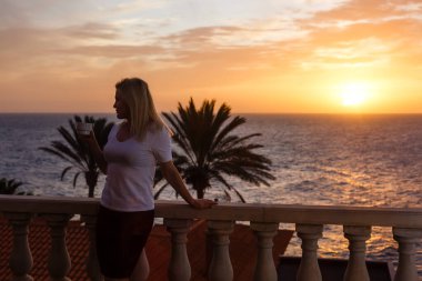 Balkondan gün batımına hayran bir kadın.