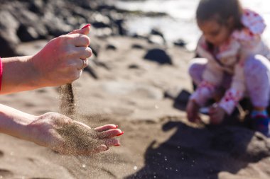 Ceket giyen küçük kız kışın bulutlu gökyüzünde kumsalda oynuyor.