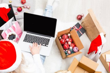 Noel çevrimiçi alışveriş merkezi manzarası. Dizüstü bilgisayarı olan kadın alıcı, ekranda boşluğu kopyala. Kadın kahve içiyor, hediyeler alıyor, Noel arifesine hazırlanıyor, hediye kutularının ve paketlerin arasında oturuyor. Kış tatili satışları