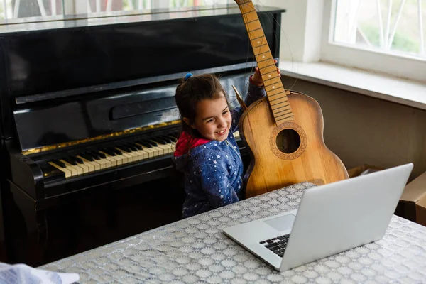셔츠를 어린이가 노트북으로 레슨을 보면서 기타치는 배우고 집에서 미소짓는 — 스톡 사진