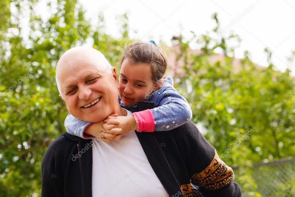 Portrait of small girl with senior grandfather in the backyard garden, standing.