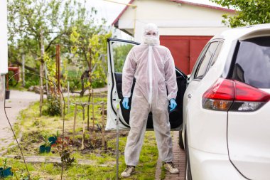 Kişisel koruyucu giysi, eldiven, cerrahi maske ve yüz maskesi takan bir adam, bir arabada oturan başka bir adam üzerinde kovid-19 koronavirüsü test ediyor..