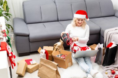 Noel partisine hazırlanıyorum. Dizüstü bilgisayardan hediye ve dekorasyon sipariş eden, hediye kutuları ve paketlerin arasında oturan, boşluğu kopyalayan bir kadın.