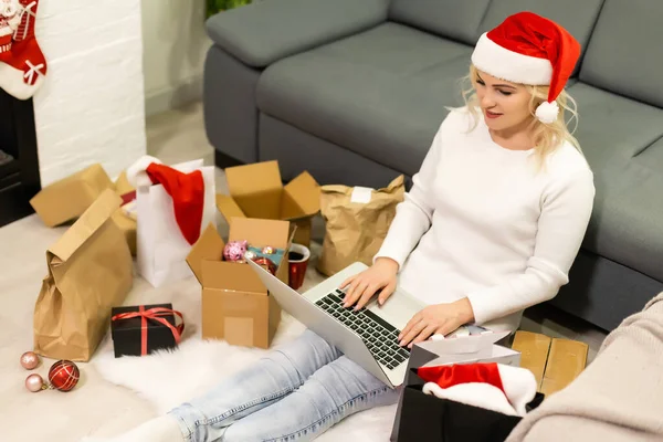 Preparing for Christmas party. Woman ordering presents and decorations on laptop, sitting among gifts boxes and packages, copy space