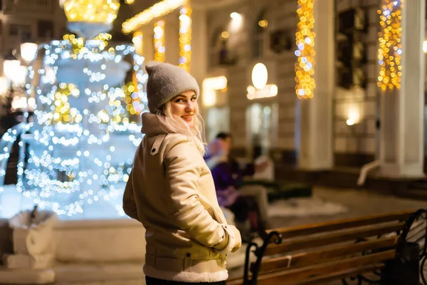 若い美しい幸せな笑顔の女の子の屋外写真は 通りにポーズの輝きを保持 背景にあるお祭りのクリスマスフェア モデルは スタイリッシュな冬のコートを着て ニットビーニー帽子 スカーフ — ストック写真