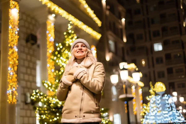 Noel festivalinde gülümseyen güzel bir genç kadının sokak portresi. Klasik, şık, kış örgü giysileri giyen bir bayan..