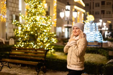 Noel festivalinde gülümseyen güzel bir genç kadının sokak portresi. Klasik, şık, kış örgü giysileri giyen bir bayan..