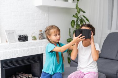 Evdeki oturma odasında iki küçük çocuğun sanal gerçeklik gözlüklerini kullanırken çekilmiş bir fotoğraf..