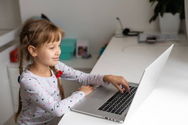 Evde bilgisayarını kullanarak internetten ders çalışan küçük bir kız.