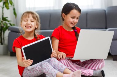 İki küçük kız dizüstü bilgisayarın önünde oturuyor ve gülüyorlar, yakın plan, olumlu duygular, internette çocuklar için eğlence.