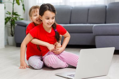 İki küçük kız dizüstü bilgisayarın önünde oturuyor ve gülüyorlar, yakın plan, olumlu duygular, internette çocuklar için eğlence.