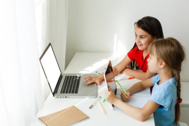 Havalı online okul. Çocuklar evde dizüstü bilgisayar kullanarak ders çalışıyor. Çevrimiçi e-öğrenme sisteminde çalışırken dizüstü bilgisayar kullanan neşeli küçük kızlar. Uzaktan öğrenme