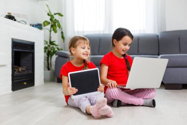 Tablet bilgisayarında oynayan küçük kızlar yerde oturuyor.