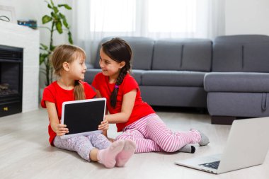 Tablet bilgisayarında oynayan küçük kızlar yerde oturuyor.