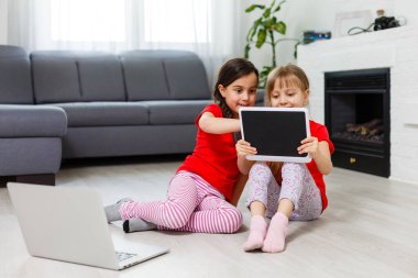 Tablet bilgisayarında oynayan küçük kızlar yerde oturuyor.