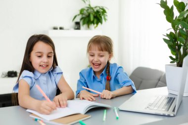 Havalı online okul. Çocuklar evde dizüstü bilgisayar kullanarak ders çalışıyor. Çevrimiçi e-öğrenme sisteminde çalışırken dizüstü bilgisayar kullanan neşeli küçük kızlar. Uzaktan öğrenme