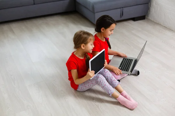 Two little girls sitting in front of a laptop and laughing, close-up, positive emotions, entertainment on the Internet for children