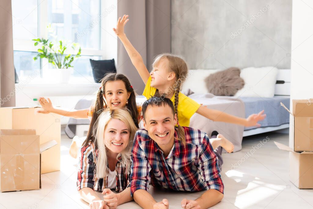 Excited young family have fun in living room unpacking cardboard boxes on moving day, happy parents play with little daughters jump out of carton package, overjoyed relocating to new home together