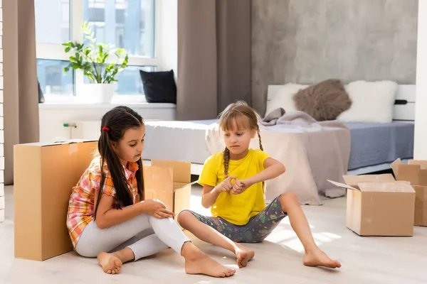 Happy family in living room. Preschool daughters sitting and help unpacking cardboard boxes belongings. Buy real estate, relocation at new modern house